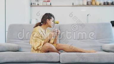 穿着浴袍的年轻女子坐在沙发上的房间里。 他坐在沙发上喝咖啡看电视。 舒适